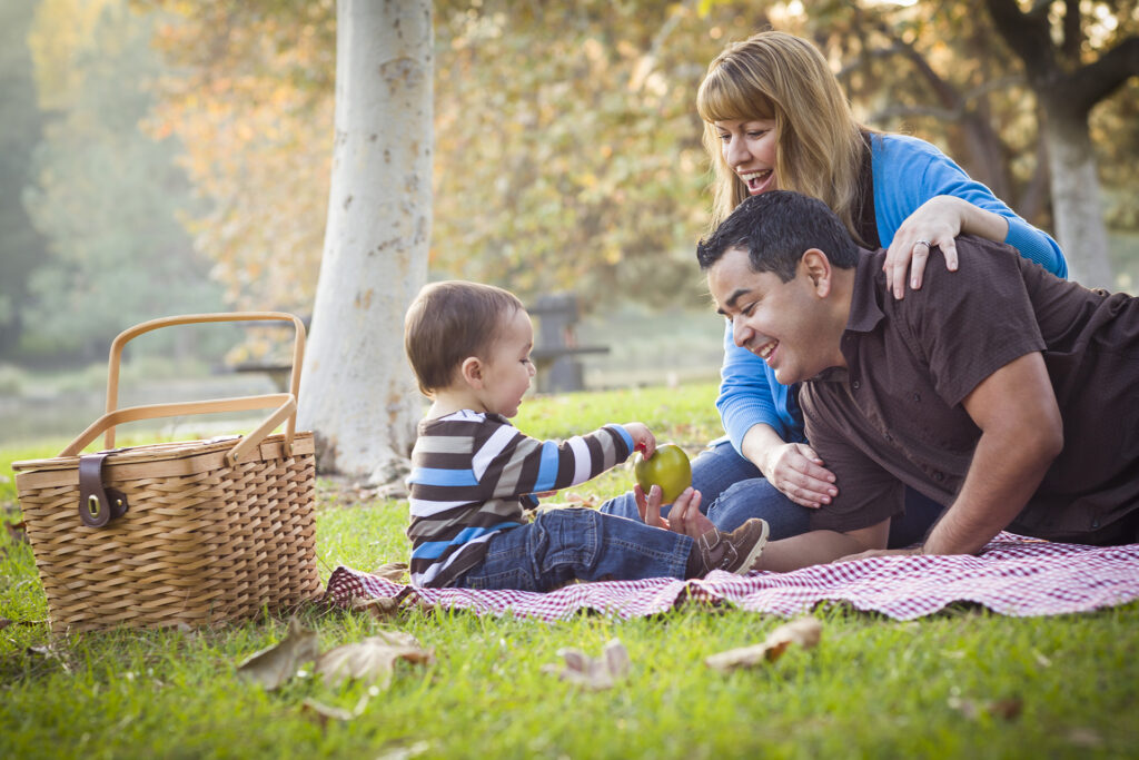 Happy Young Family Having a Picnic In The Park.